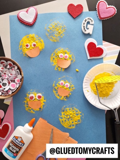 A blue paper with six yellow chick faces stamped on it, surrounded by googly eyes, heart shapes, a bottle of glue, a fork, and craft supplies. The handle @GLUEDTOMYCRAFTS is displayed at the bottom.