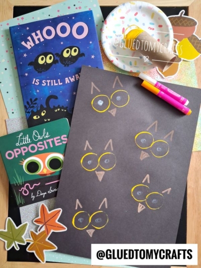 Children’s owl-themed craft setup with two books, paper owls drawn on black paper, markers, paper leaves, a glue stick, and acorn cutouts. A small paper plate and a charming toilet roll stamped owl are also included. @GLUEDTOMYCRAFTS text is visible.