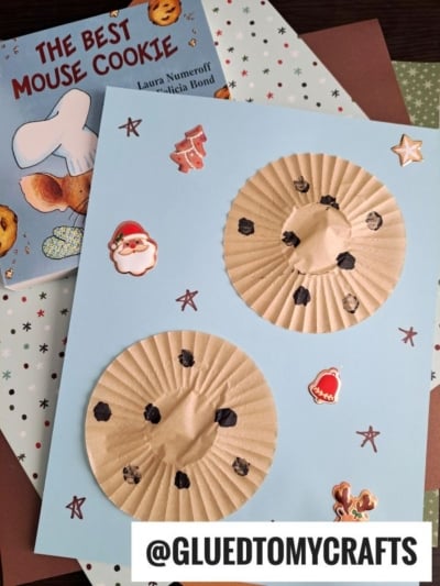 A mouse cookie craft made with brown cupcake liners, black dots for chocolate chips, and small stickers on blue paper—perfect for cupcake liner card crafts. The book “The Best Mouse Cookie” is in the corner. Text: @GLUEDTOMYCRAFTS.