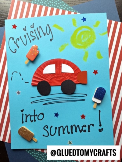 A handmade summer-themed card features a red paper car, popsicle stickers, a yellow sun, and the words “Cruising into summer!” on blue paper, atop red and blue striped backgrounds. The handle @GLUEDTOMYCRAFTS is at the bottom.