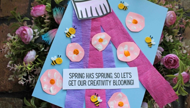 A spring-themed craft featuring pink and purple paper flowers, small decorative bees, and a “Spring has sprung, so let’s get our creativity blooming!” sign on a blue background—perfect for pairing with Spring Printables.