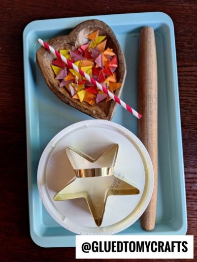 A tray holds a wooden heart dish with origami stars and a striped straw, a rolling pin, a white container lid, and a gold star-shaped cutter. The handle @GLUEDTOMYCRAFTS is displayed at the bottom.
