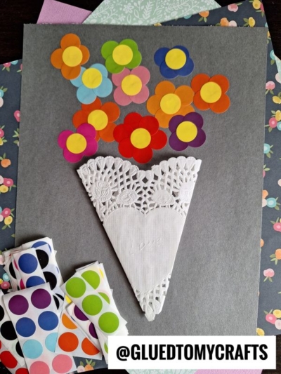 A paper doily and colorful paper flowers showcase creative coding label crafts on a grey surface.