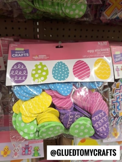 A package of colorful egg-shaped stickers in yellow, blue, green, and purple with various patterns, labeled egg stickers from Easter Crafts, hanging on a store display. @GLUEDTOMYCRAFTS text at the bottom.