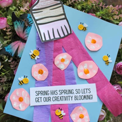 A colorful craft project featuring a paper paintbrush, purple and pink paper strips, flowers, and bees, with the text “Spring has sprung, so let’s get our creativity blooming!” and “Free Printable” at the bottom.