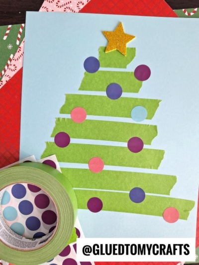 A Christmas tree made from green tape strips on blue paper, decorated with purple and pink dot stickers like coding label crafts, and topped with a yellow star. A roll of green tape and sheets of dot stickers are beside it. @GLUETOMYCRAFTS is at the bottom.
