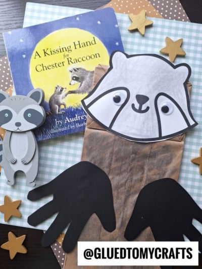 Children’s craft inspired by A Kissing Hand for Chester Raccoon book; perfect for back to school story time, it features a raccoon puppet made from a paper bag, black cut-out hands, a raccoon cutout, star shapes, and patterned paper in the background.