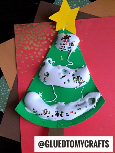 A Christmas tree craft made from green paper, marshmallows, white glue, sequins, and a yellow star on top—perfect for holiday puffy paint crafts. Displayed on layered colored paper backgrounds. Text reads @GLUEDTOMYCRAFTS.