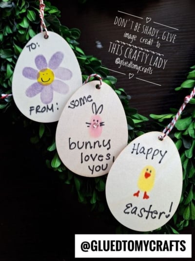 Three wooden egg-shaped tags with Easter designs: a purple flower with TO: FROM:, a bunny with Some bunny loves you, and a chick with Happy Easter!, all on string against a dark background.