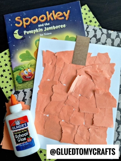 A children’s pumpkin book, Halloween-themed paper, a glue bottle, and an orange paper craft with torn pieces are displayed on a dark surface—perfect inspiration for FALL CRAFTS FOR KIDS. The Instagram handle @GLUETOMYCRAFTS appears at the bottom.