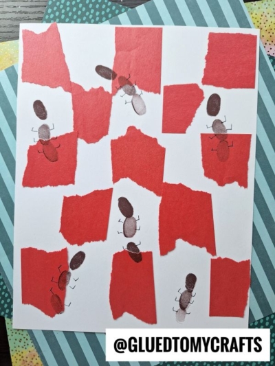 A white paper with torn pieces of red paper glued on, creating a collage. Several ants made from brown thumbprints and drawn legs are scattered across the page. The background includes patterned craft paper.