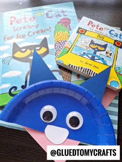 Two Pete the Cat books are shown with a blue paper plate craft shaped like Pete’s face, featuring paper ears, googly eyes, and a paper nose. A watermark reads @GLUEDTOMYCRAFTS in the bottom right corner.