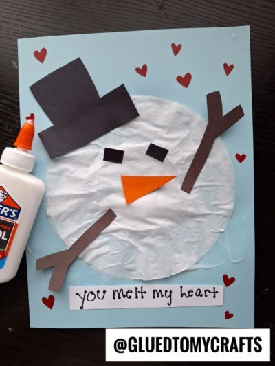 A childrens snowman craft made from tissue paper, construction paper, and glue, with red heart shapes around it. Below is a handwritten note: “You melt my heart” and the username @GLUEDTOMYCRAFTS.