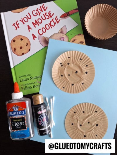 A copy of If You Give a Mouse a Cookie, glue, black paint, Q-tips, cupcake liners, and blue paper are arranged on a table, perfect for a back to school story time and craft activity.