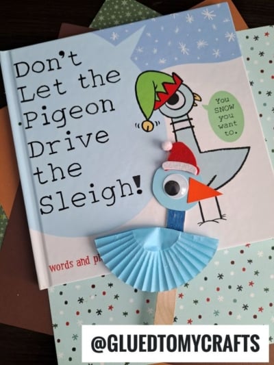 A children’s book titled Don’t Let the Pigeon Drive the Sleigh! is pictured with a festive pigeon craft—made from a blue cupcake liner, googly eye, red hat, and orange beak—showcasing fun cupcake liner card crafts. @GLUETOMYCRAFTS text appears.