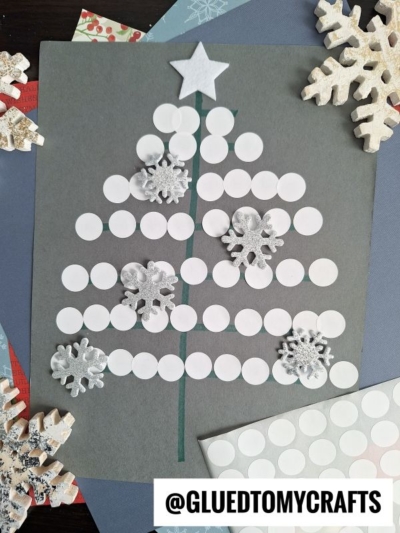 A simple Christmas tree is made from white sticker dots on dark paper, topped with a white star and decorated with snowflake embellishments—perfect for coding label crafts. Large decorative snowflakes and paper surround the artwork.