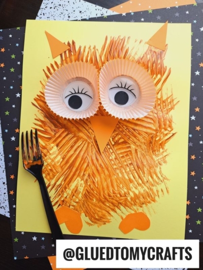 A handmade owl art project on yellow paper makes a fun addition to FALL CRAFTS FOR KIDS, using orange paint, a black fork for texture, cupcake liners for eyes, and orange paper shapes. A @GLUEDTOMYCRAFTS tag is at the bottom.
