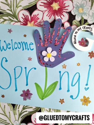 A spring-themed craft features a blue paper with Welcome Spring! written in blue and green. A purple handprint with a flower and glitter decorates the page. Embroidered flowers and @GLUEDTOMYCRAFTS appear at the bottom.