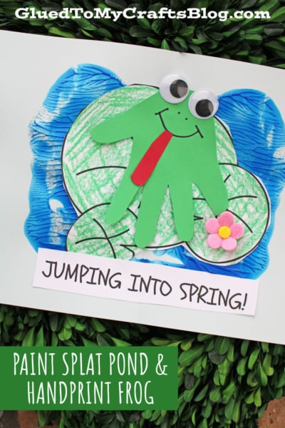 A kids’ craft featuring a green handprint frog with googly eyes and a red tongue on a blue paint splat pond, decorated with a pink felt flower. Text reads “Jumping Into Spring!” and “Paint Splat Pond & Handprint Frog.”.