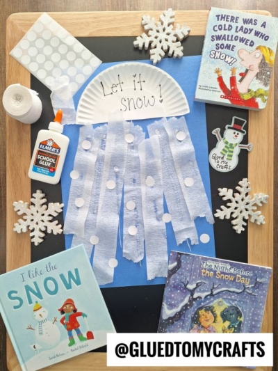 A flat lay shows a kids’ winter craft of a paper plate reading “Let it snow!” with tissue paper and paper dots for snow, surrounded by snowflake decorations, coding label crafts, three winter books, white glue, and the @GLUEDTOMYCRAFTS logo.