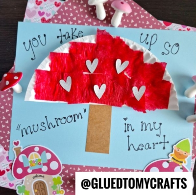 A craft project shows a red paper mushroom with silver hearts on a blue background. Handwritten text reads You take up so mushroom in my heart. Decorative mushrooms and houses surround the artwork.