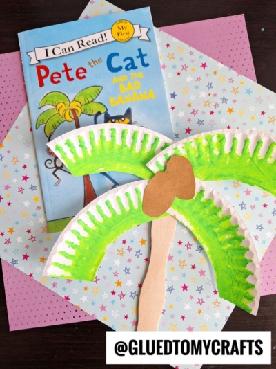 A children’s book titled Pete the Cat and the Bad Banana is placed on pastel star-patterned paper next to a handmade palm tree craft made from a painted paper plate, brown paper, and a craft stick. Text: @GLUEDTOMYCRAFTS.