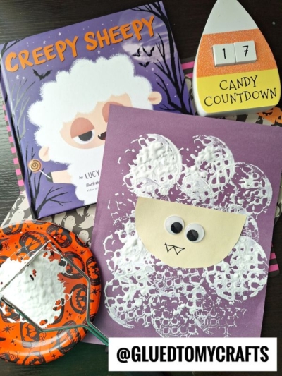 A children’s craft scene featuring a “Creepy Sheepy” book, a sheep art project made with bubble wrap paint and googly eyes on purple paper, a Halloween countdown, and a potato masher stamped craft on a Halloween-themed plate.