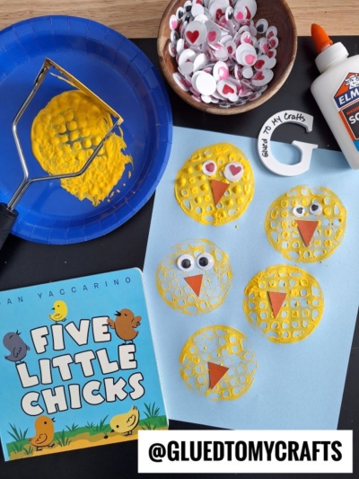 A children’s craft setup inspired by Five Little Chicks shows yellow chick faces stamped on blue paper using a potato masher, googly eyes, heart stickers, glue, and a bowl of craft eyes.