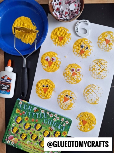 A childrens craft activity displays yellow chick faces made with textured paint, googly eyes, and beaks on white paper. Supplies include glue, a potato masher, and a book titled Ten Little Chicks.