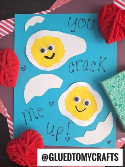 A blue card features two egg shapes made from white paper and yellow sponges with googly eyes and smiles. Surrounding text reads You crack me up! This is one of the cutest Sponge Painting Ideas for Kids, with red yarn hearts and a green sponge nearby.