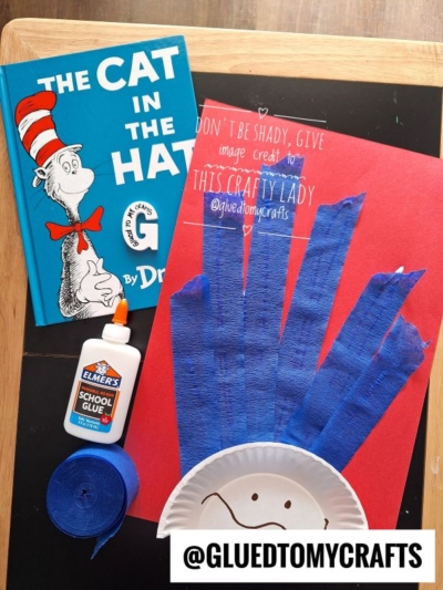 A Cat in the Hat book, white glue, blue crepe paper, and a red sheet with blue paper strips and a paper plate face create a Cat in the Hat craft. @GLUEDTOMYCRAFTS is written at the bottom.