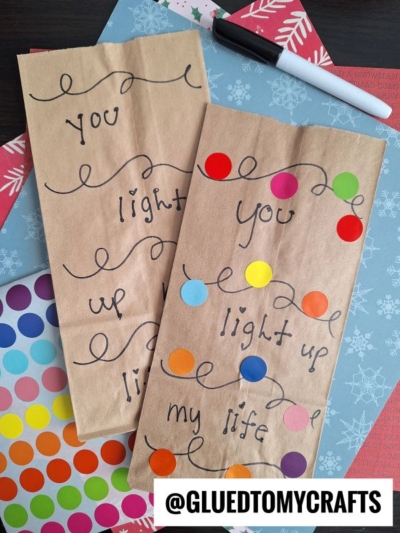 Two brown paper bags with handwritten text reading "You light up my life," decorated with colorful dot stickers—perfect for coding label crafts. A black marker, sticker sheets, and patterned paper are nearby. @GLUEDTOMYCRAFTS at the bottom.