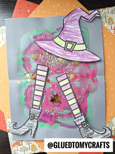 A Halloween-themed PAINT SPLAT CRAFT features a witch’s hat and striped legs on gray paper, decorated with colorful paint smears, glitter, and star sequins, layered over orange patterned paper. @GLUEDTOMYCRAFTS is at the bottom.