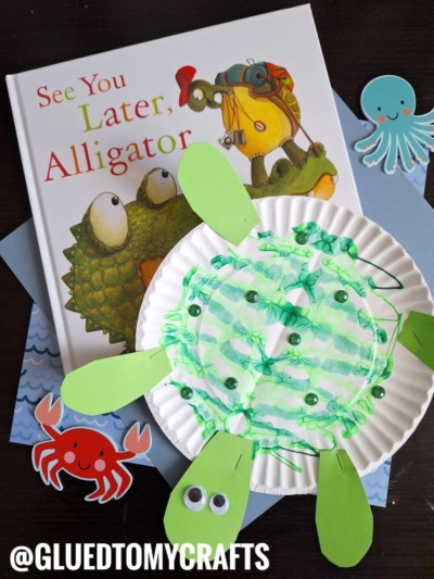 A children's book titled See You Later, Alligator is surrounded by playful paper crafts: a green turtle from a paper plate, an octopus, and a crab. The colorful creatures with googly eyes bring PAINT SPLAT CRAFTS fun to storytime.