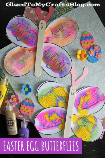 Two colorful butterflies crafted from decorated Easter eggs, paper, and craft sticks are displayed on patterned paper, surrounded by felt flowers, glitter glue bottles, and Easter egg art. Text reads “EASTER EGG BUTTERFLIES.”.