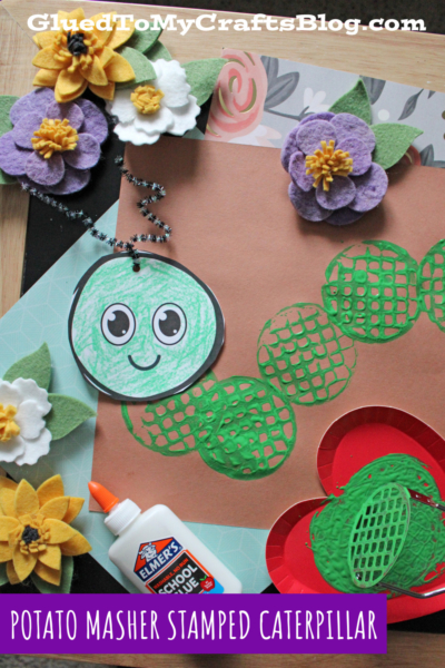 A caterpillar craft made from green circles stamped with a potato masher, with a smiling face, felt flowers, glue, and colored paper. Text reads Potato Masher Stamped Caterpillar.
