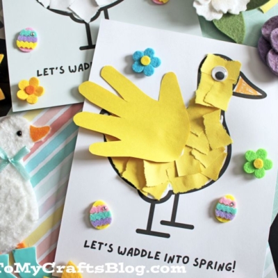 A spring-themed craft display features a yellow duck made from a child’s handprint, felt flowers, a felt duck, and colorful decorations on cards reading “Let’s waddle into spring!”.