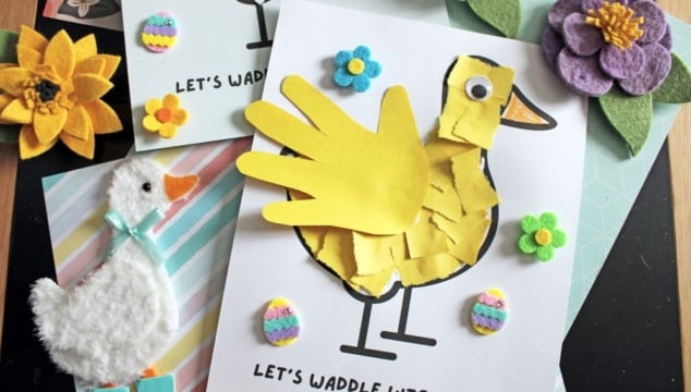 A spring-themed craft display features a yellow duck made from a child’s handprint, felt flowers, a felt duck, and colorful decorations on cards reading “Let’s waddle into spring!”.