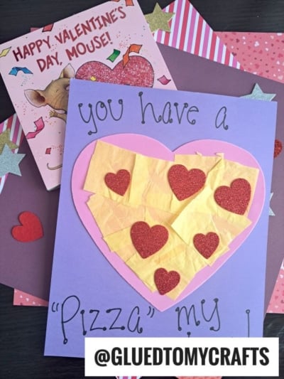 A handmade Valentines card with a large pink and yellow heart, decorated with red glitter hearts, is perfect for heart shaped crafts. The words "You have a pizza my heart" add charm, with valentines cards and starry craft paper in the background.