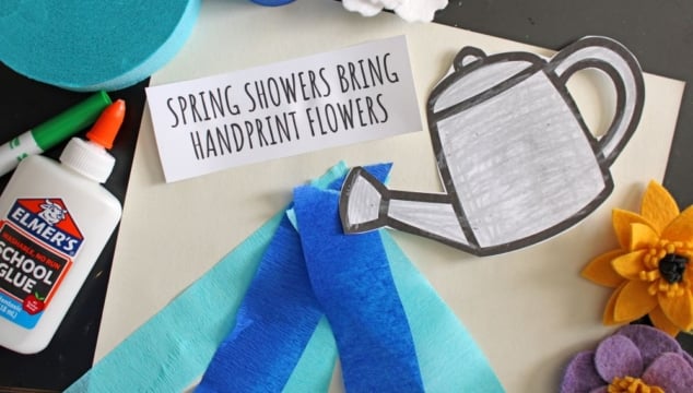A craft scene with a glue bottle, blue and yellow felt flowers, blue crepe paper strips, a paper watering can, and a card reading “Spring Showers Bring Handprint Flowers,” features fun Spring Printables on a white background.