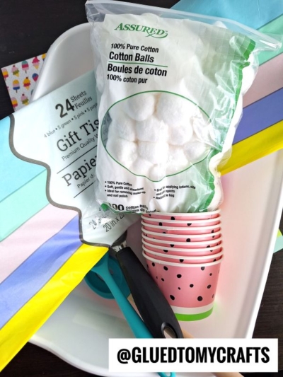 A plastic tray holds a pack of cotton balls, pastel-colored tissue gift wrap, strawberry-printed paper cups, and craft tools. A label reads @GLUEDTOMYCRAFTS at the bottom right.