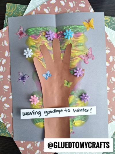 A colorful spring craft shows a hand cutout as a tree trunk with flowers and butterflies on a bright, crayon-drawn, paint splat crafts-inspired tree. A label reads “Waving goodbye to winter!” and the image is branded @GLUEDTOMYCRAFTS.