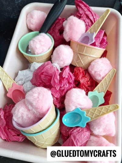 Plastic ice cream cups and pastel-colored spoons filled with pink pom-poms and crumpled tissue paper, arranged in a tray. The Instagram handle @GLUEDTOMYCRAFTS appears at the bottom.