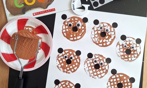 A children’s craft setup features a Bear Counts book, glue, googly eyes, black dot stickers, and a potato masher stamped craft with brown bear faces, plus a finished bear face and supplies displayed on the table.