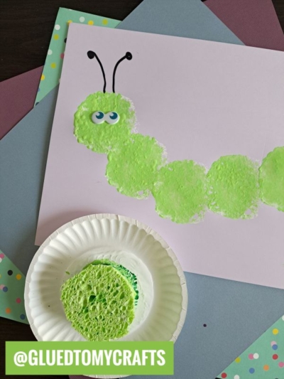 A fun INSECT CRAFT IDEA, this caterpillar is made from green sponge paint prints on white paper, with black antennae, googly eyes, and a paint-covered sponge on a plate. Colorful papers brighten the background.