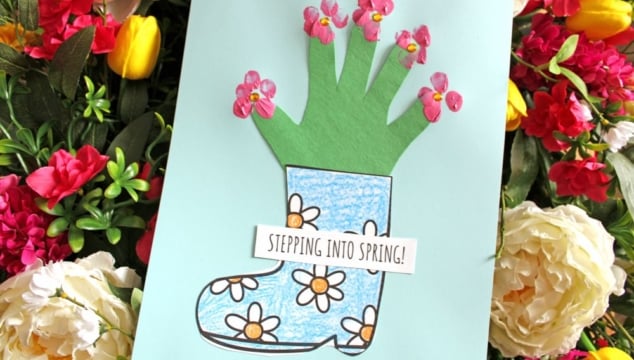 A handmade card shows a blue rain boot with drawn flowers and a green handprint sprouting pink flower stickers, with a sign reading STEPPING INTO SPRING! surrounded by colorful real flowers.