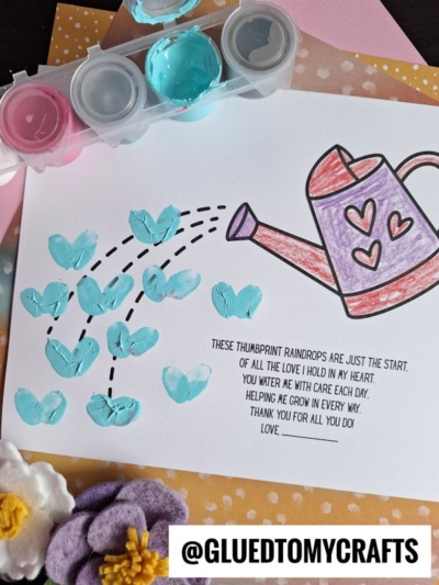 A thumbprint watering can craft for children features blue thumbprint raindrops falling from a colored watering can, with a sweet poem about love and growth. Paint pots and felt flowers add charm. @GLUEDTOMYCRAFTS is written at the bottom.
