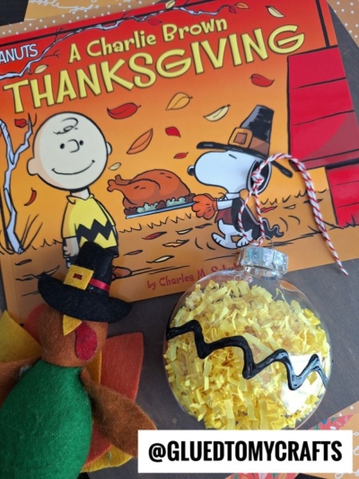 A Charlie Brown Thanksgiving book with a felt turkey toy and a clear ornament filled with yellow shredded paper—perfect for FALL CRAFTS FOR KIDS. A label reading @GLUEDTOMYCRAFTS is in the bottom right corner.