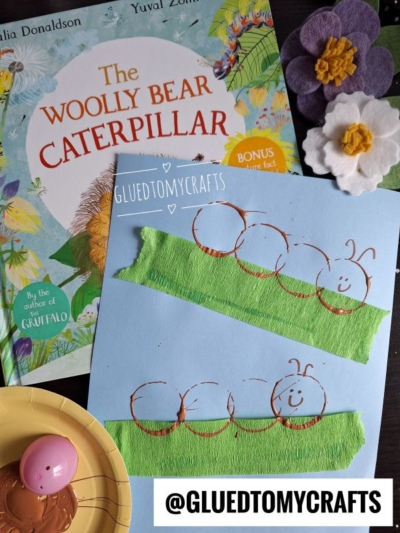 A children’s book titled The Woolly Bear Caterpillar, felt flower crafts, and a blue paper with a caterpillar made from brown paint circles using Plastic Egg Stamp Crafts on green crepe strips are shown. Supplies and @GLUEDTOMYCRAFTS tag are visible.
