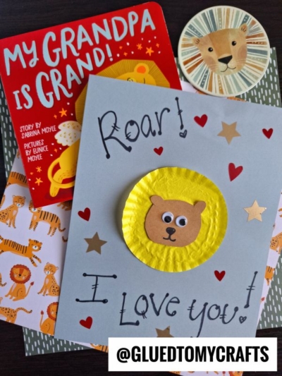 A handmade cupcake liner card craft with Roar! I Love You! and a bear face, a lion sticker, My Grandpa Is Grand! book, and animal-themed paper. Instagram handle @GLUEDTOMYCRAFTS is at the bottom.